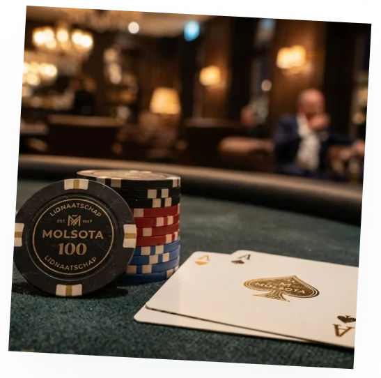 Een stapel gekleurde pokerfiches met een Molsota fiche vooraan en twee azen op een pokertafel.